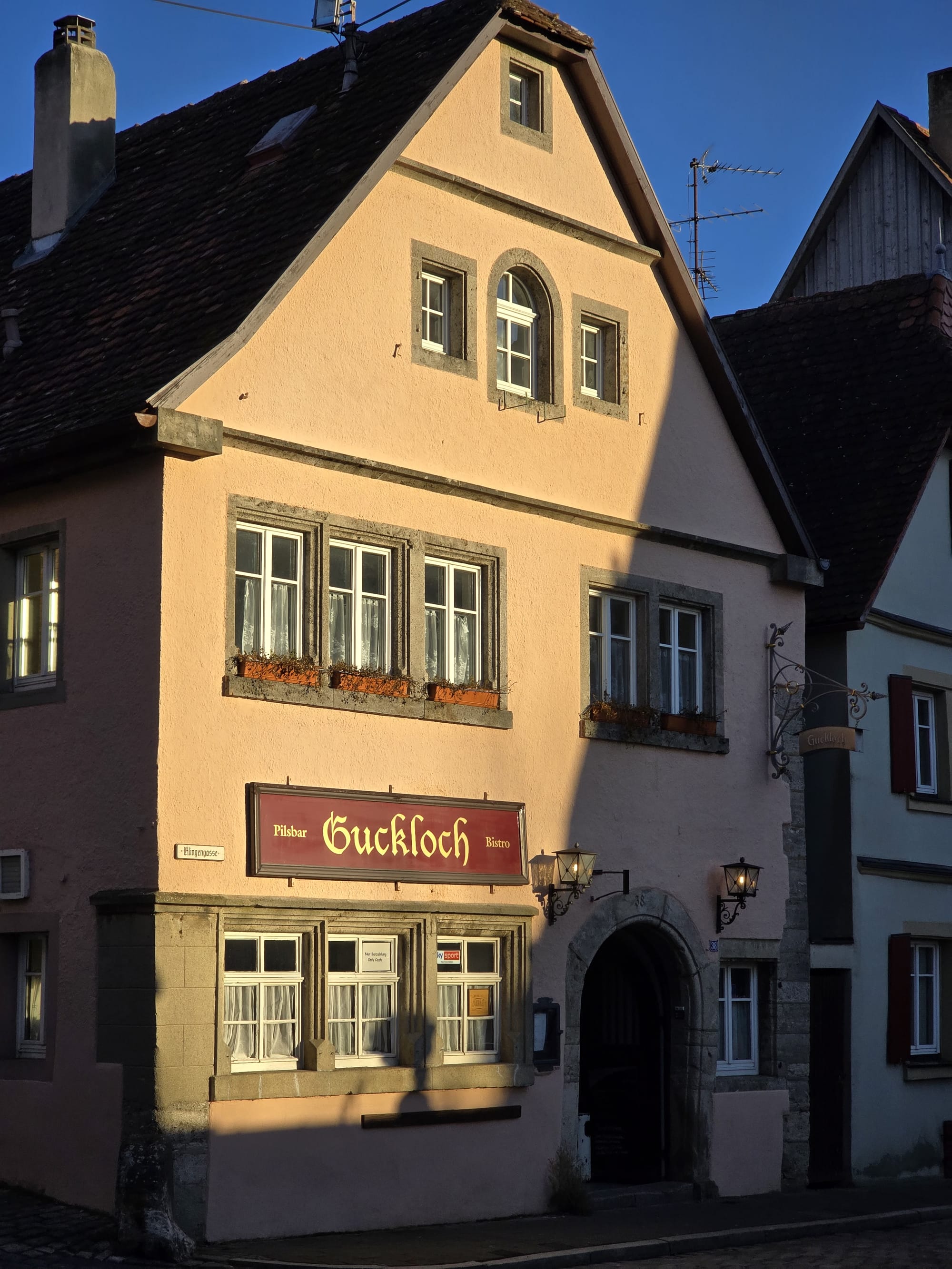 A picture of an old building with the sun shining on it. In the front of the building there is a sign that has the name of the bistro written on it. It is called the "Guckloch" Bistro.